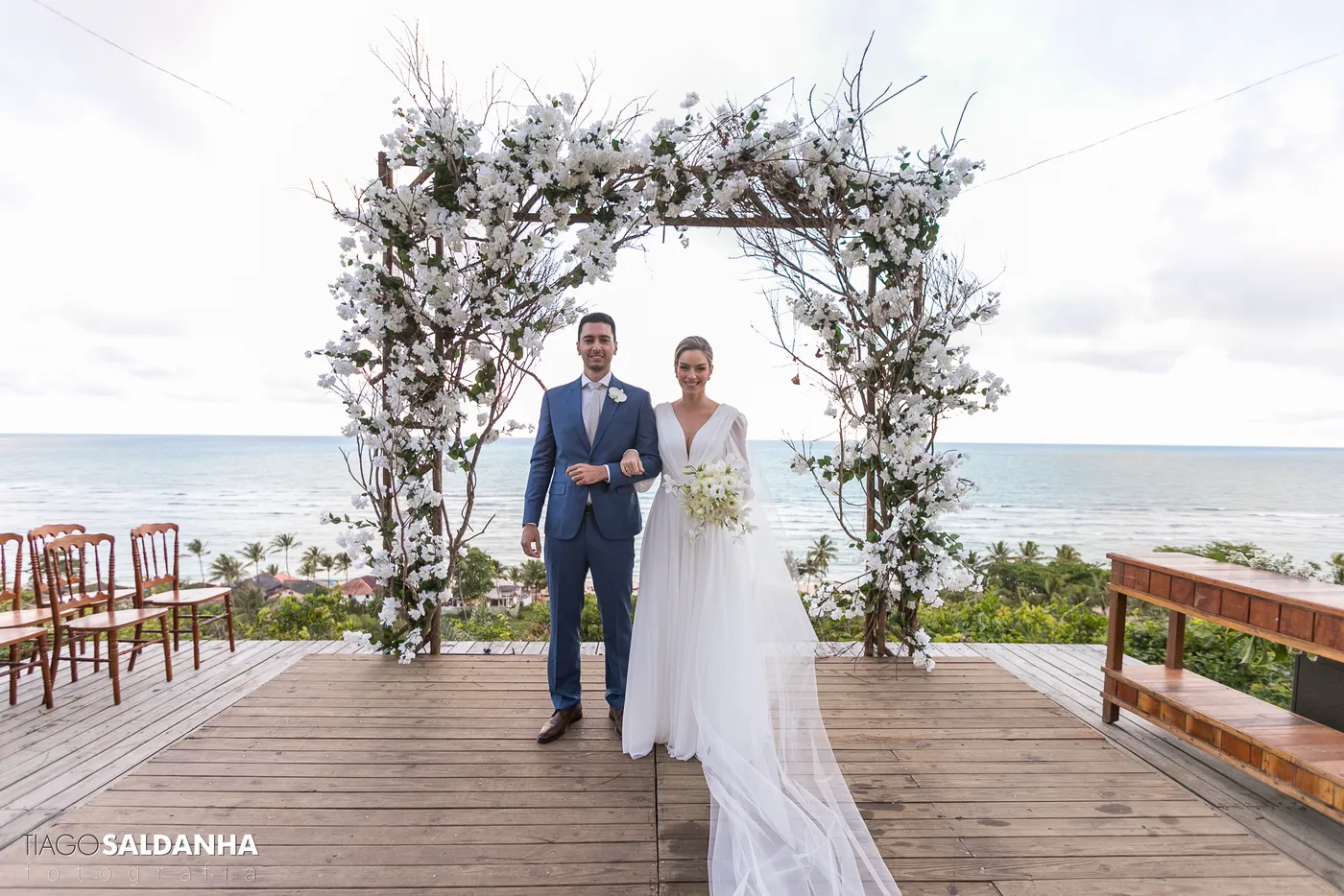 Noivos sob o arco de flores, com o mar ao fundo